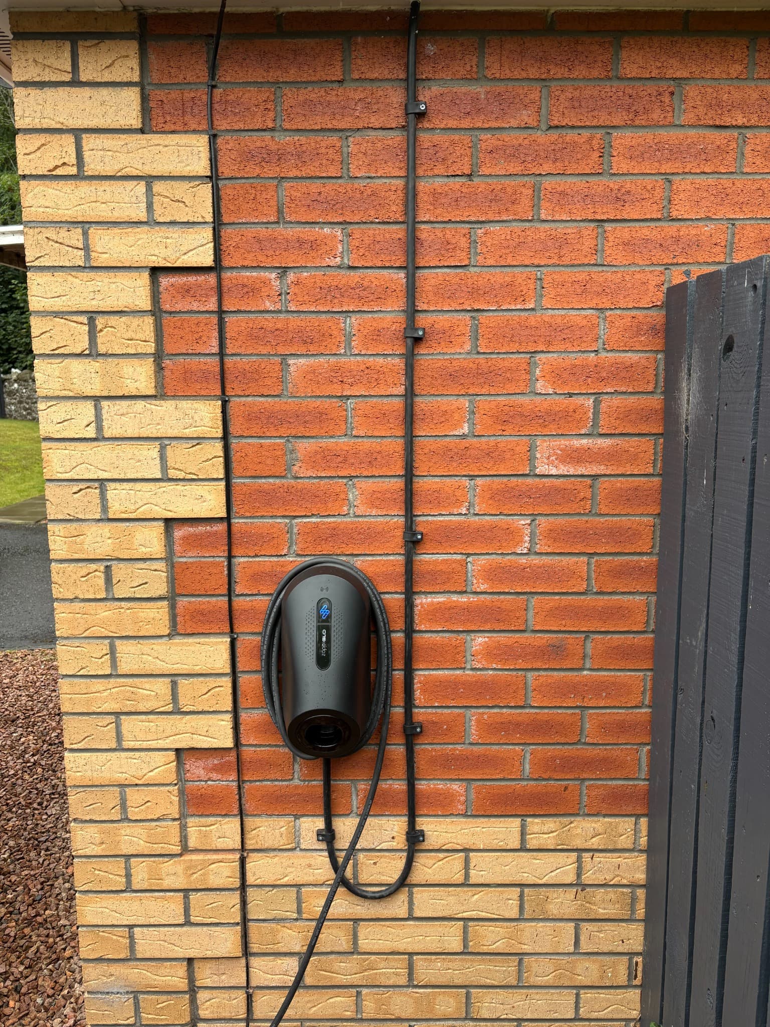 Installed myenergi Zappi EV charger with its cable arranged on a brick wall